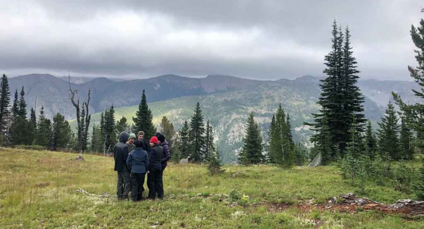 a group of students stand in a mountain meadow with a mountainous landscape in the background